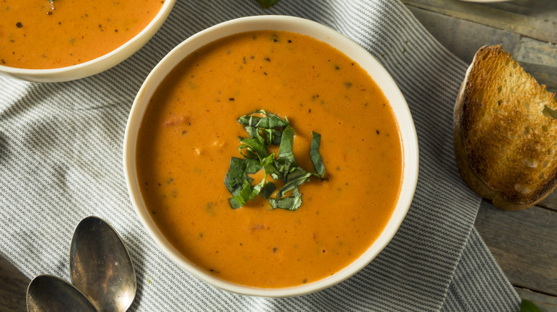 Bowl of tomato soup with fresh basil garnish, next to slice of toast