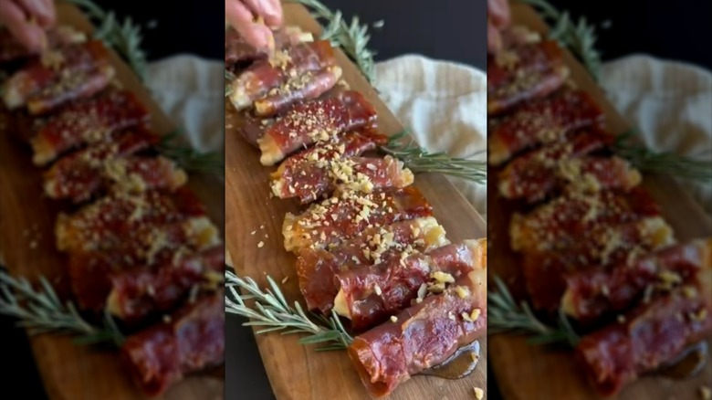 Prosciutto Boursin roll ups on wooden serving board, garnished with chopped nuts and rosemary sprigs