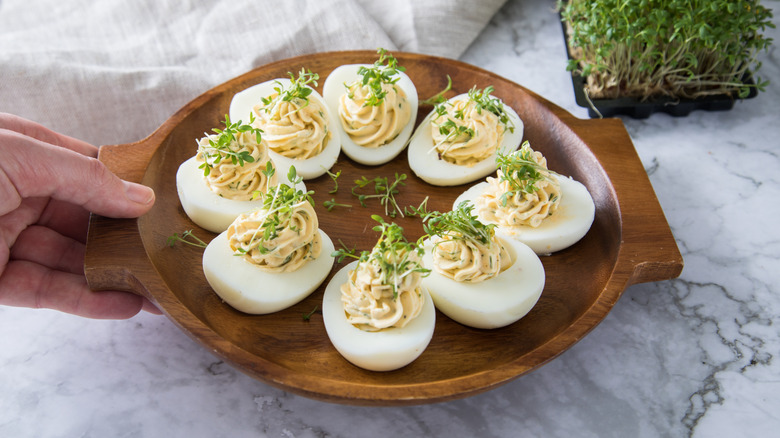 Hand placing down plate of deviled eggs garnished with cress