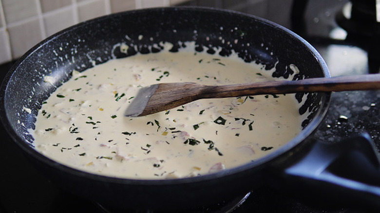 Making creamy pasta sauce with herbs and bacon in skillet
