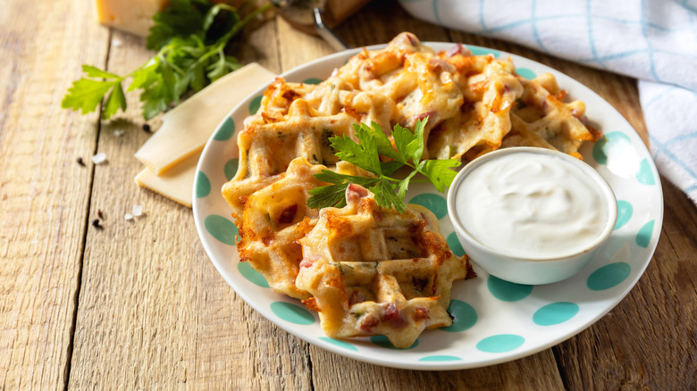 Savory cheese waffles on plate with pot of creamy dip and sprig of fresh parsley