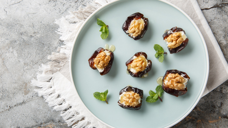 Cream cheese and walnut-stuffed dates on blue plate with mint sprigs