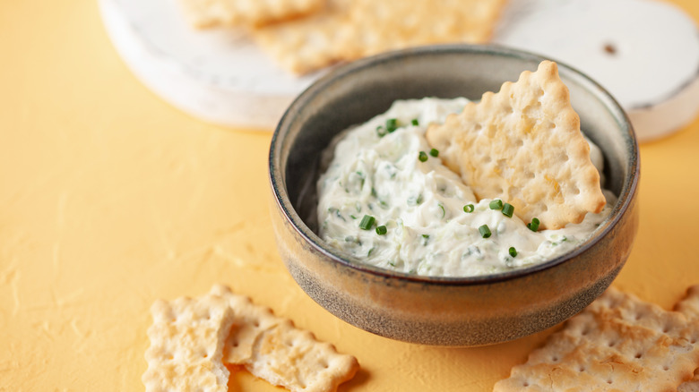 Bowl of creamy herb dep with cracker dunked in