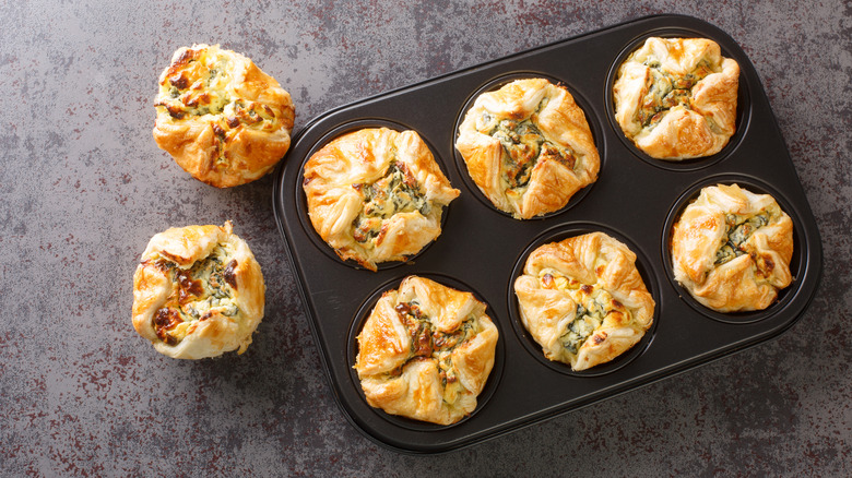 Muffin tray containing puff pastry tartlets filled with spinach and cream cheese