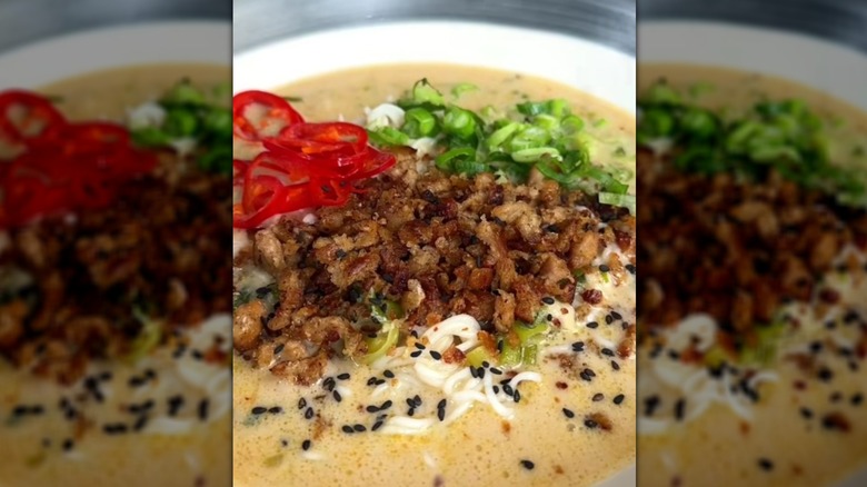 Close up of bowl of ramen topped with crumbled sausage, sliced red chili peppers, and green onions