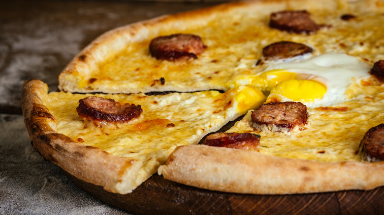 Sliced breakfast pizza with sausage and egg on wooden serving board