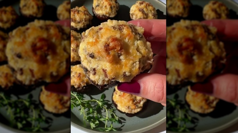 Hand holding cheesy sausage-stuffed mushroom over plate