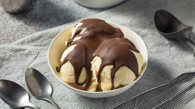 A vanilla sundae topped with chocolate shell syrup in a white bowl