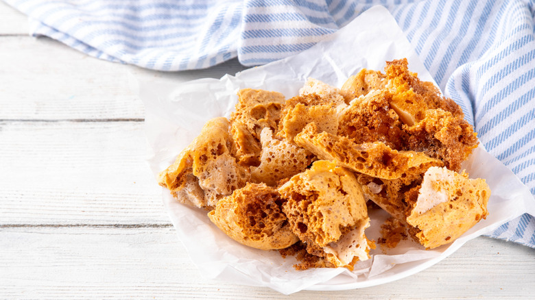 Honeycomb toffee placed on white plate on top of a wooden table near a striped napkin
