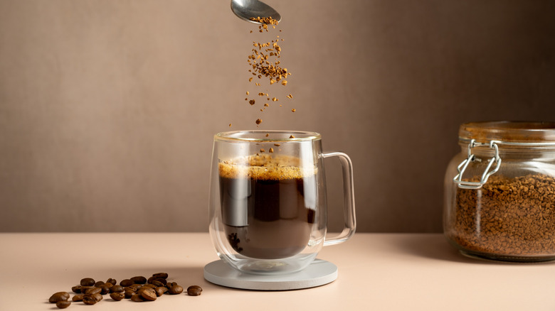 Instant coffee grounds being poured from a spoon into a clear mug