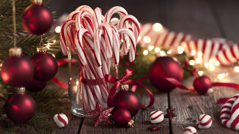 Candy canes ties by a red bow in a clear cup, surrounded by various minds and Christmas ornaments