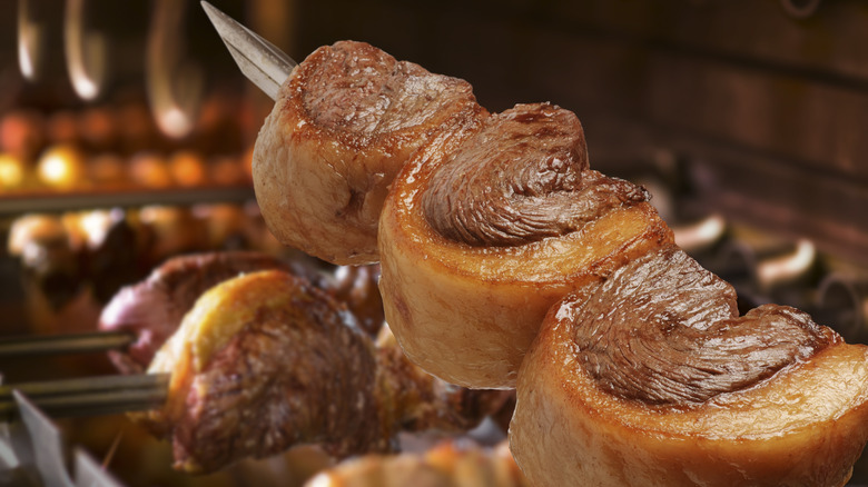 A picanha skewer being held over a flaming grill