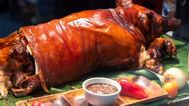 A whole-roasted pig atop a bed of leaves with accoutrements