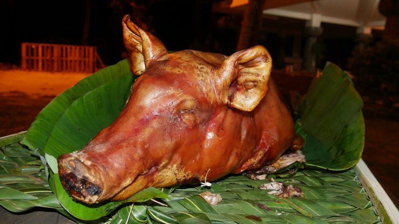 The whole head of a roasted hog atop banana leaves