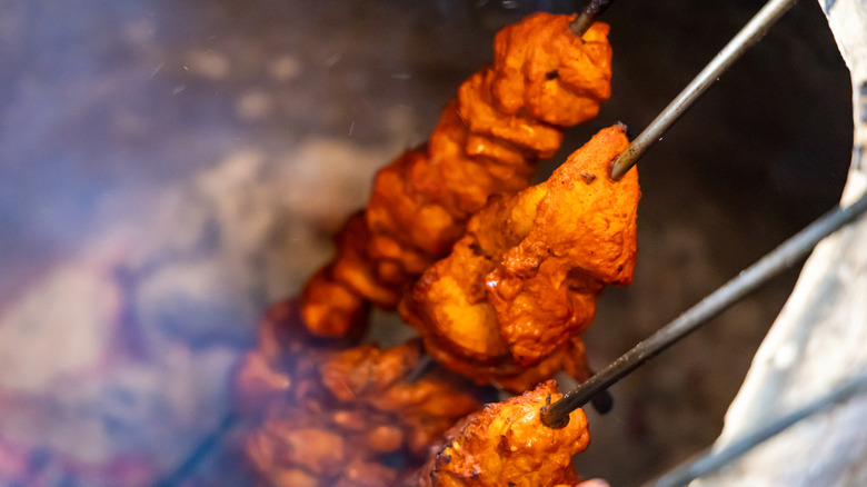 Tandoori chicken skewers cooking inside of a tandoor