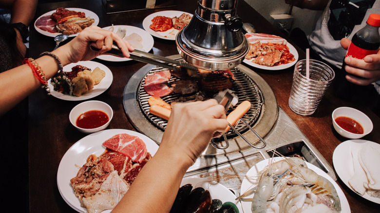 Several people grilling meat at a Korean barbecue restaurant
