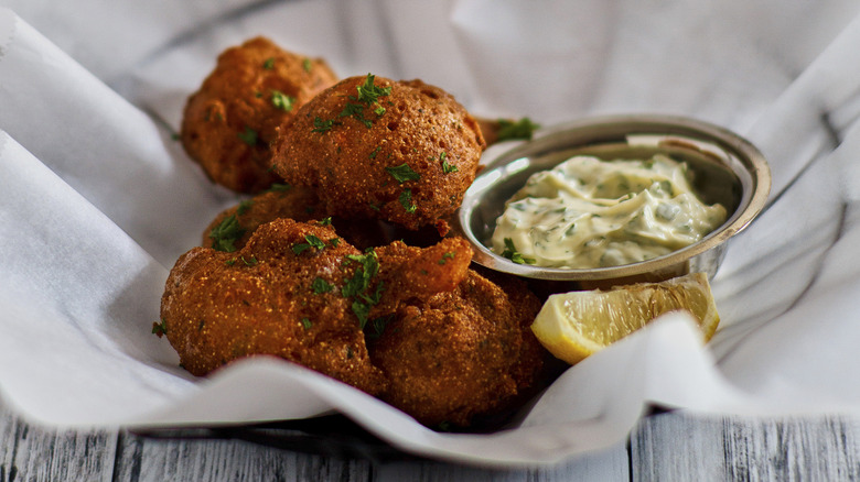 Crispy lobster fritters in parchment-lined basket with creamy sauce and lemon wedge
