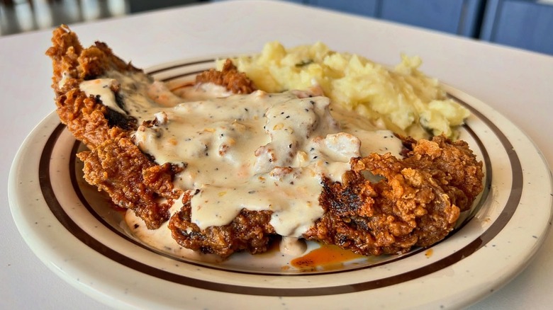 Chicken fried steak with gravy and mashed potatoes on white and brown plate