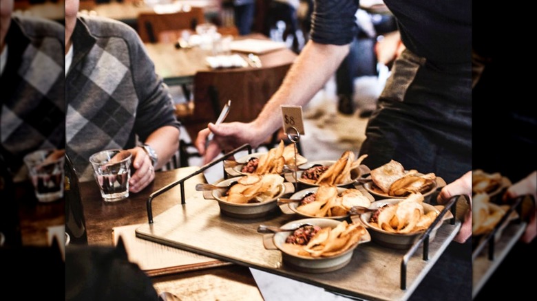 Member of wait staff carrying tray of small plates between tables