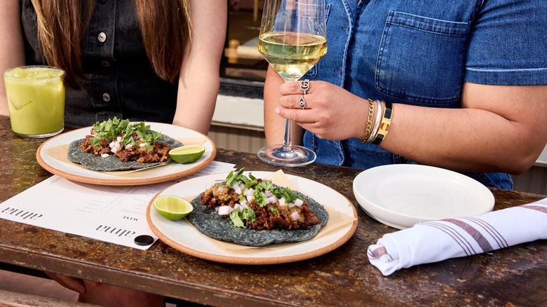 Unidentified diners with wine and cocktail, and two plates with a single taco each
