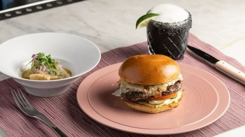 Burger and a cocktail on a pink and white table and setting