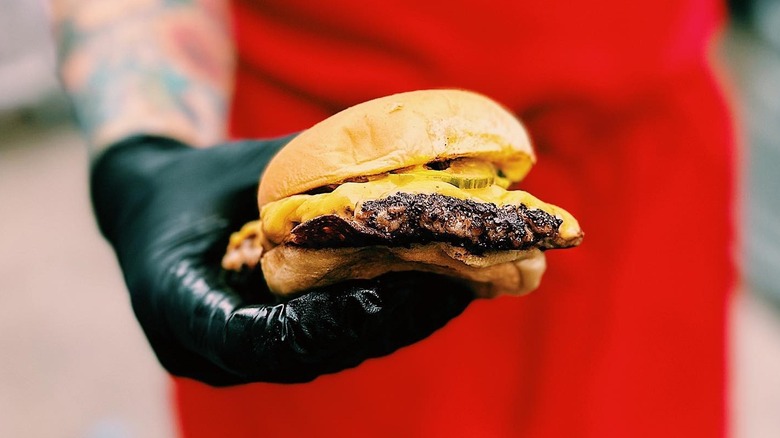 Gloved hand holding BBQ slider in front of red apron