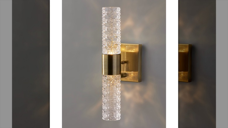 A textured glass and brass wall sconce illuminated on a wall
