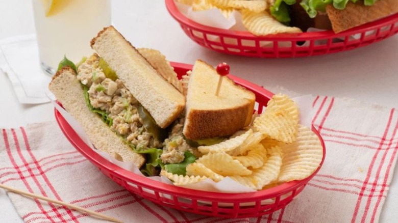 Chicken salad sandwich with chips in a red basket on a white and red tablecloth