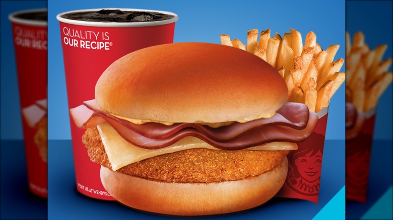 Still image of Chicken Cordon Blue sandwich in front of soda and fries on blue background