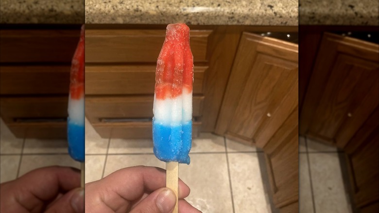 A hand holds a tri-colored Original Bomb Pop in a kitchen.