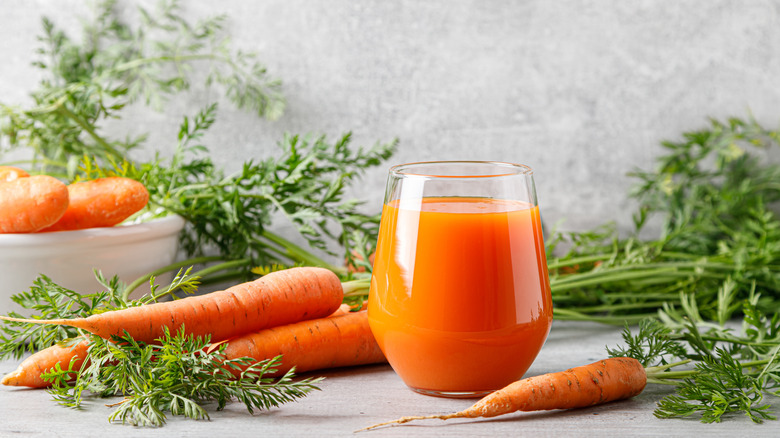 Class of carrot juice with fresh carrots in the background