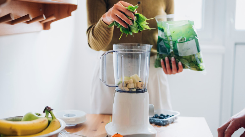 Woman preparing smoothie with fruit and greens