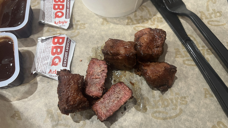 Arby's steak nuggets on a piece of paper with some barbecue sauce to the side