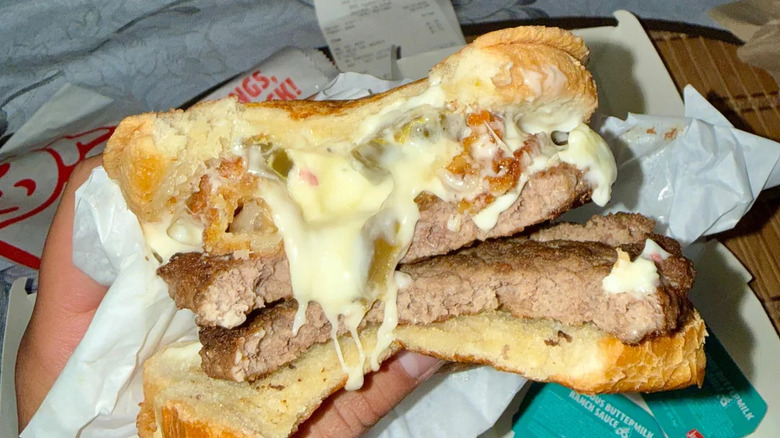 A person holding a partially eaten Jack in the Box Hot Mess Burger
