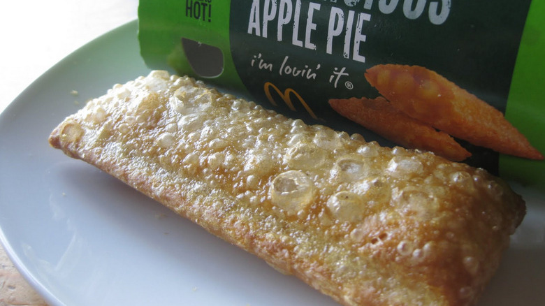 McDonald's fried apple pie sitting on a plate next to the cardboard sleeve it came from