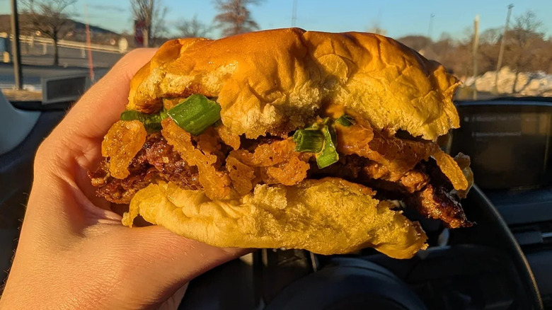 A hand holding a K Shack BBQ Burger featurings crispy onions and green onions