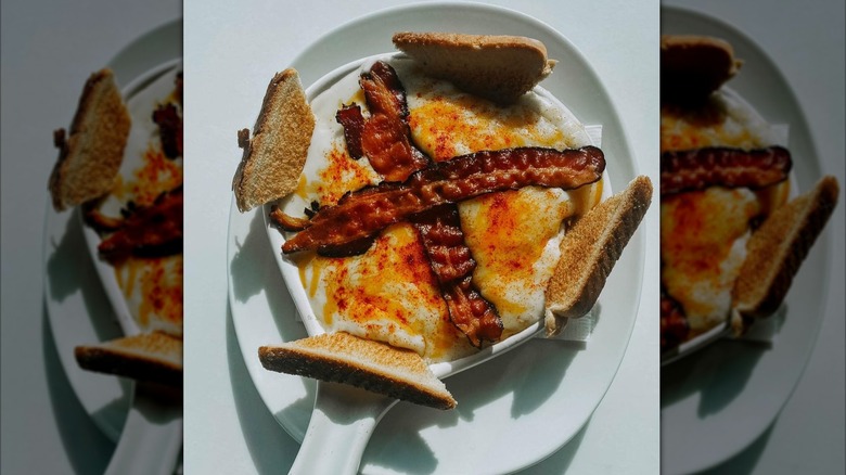 Hot brown on a platter, topped with cheese and bacon, served with toast on a white platter