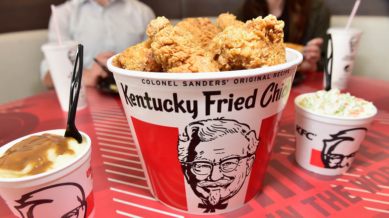 Bucket of KFC fried chicken beside sides of mashed potatoes and coleslaw