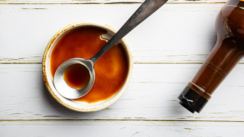 Worcestershire sauce in a bowl with a spoon next to a bottle of sauce