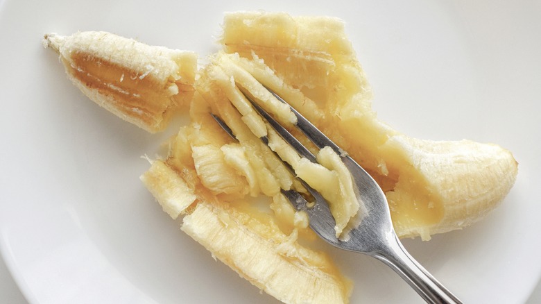 Mashing banana with fork on white plate