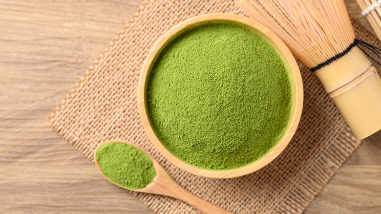 Matcha powder in bowl next to wooden spoon and whisk