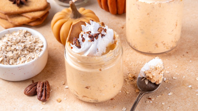 Jar of pumpkin overnight oats topped with whipped cream and chopped walnuts