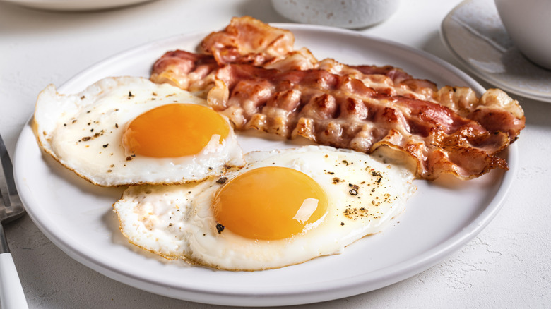 Fried sunny side eggs with bacon on white plate