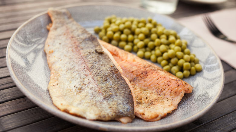 fried trout filet on a plate with green peas