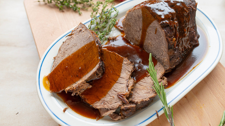 close up of roast beef on white dish with gravy and herbs