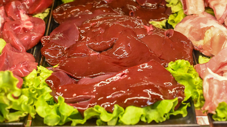 Fresh veal liver with leafy greens in the butcher shop, close up