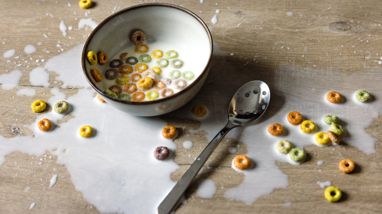 Messy bowl of cereal spilled out onto a wooden tabletop