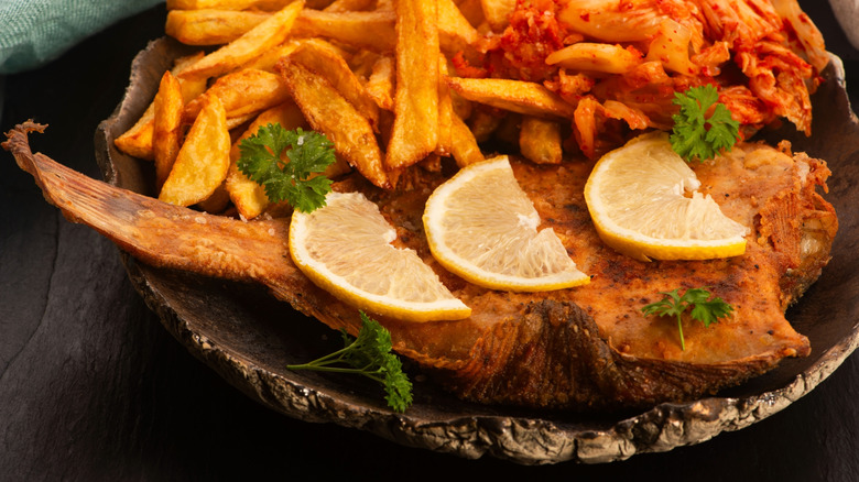 Breaded flounder with fries and kimchi on a black table