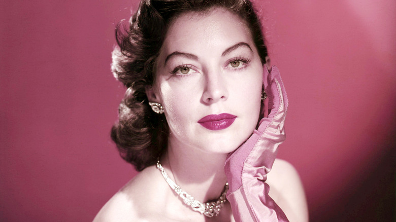 Image of Ava Gardner with a pink gloved hand to her face against pink background