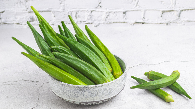 Green okra in a bowl against a white background